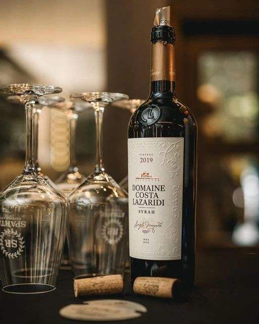 Syrah Domaine Costa Lazaridi Rotwein Flasche mit Weingläsern und Korken auf Holztisch