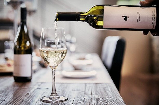 Weißwein in einem Glas mit Flasche im Hintergrund auf einem Holztisch.