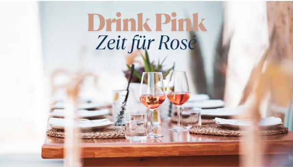 Zwei Gläser Roséwein auf einem Holztisch mit Tischgedeck und Deko.