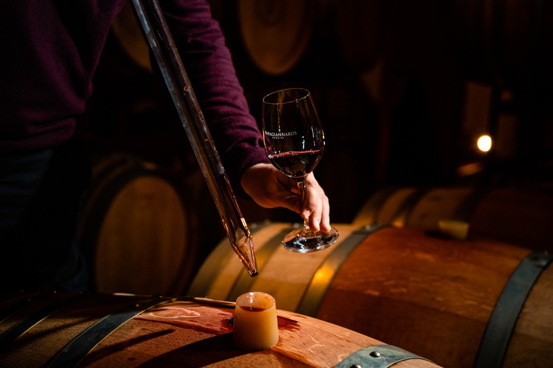 Glas mit Rotwein in einer Weinlagerung mit Holzfässern und einem Weintester.