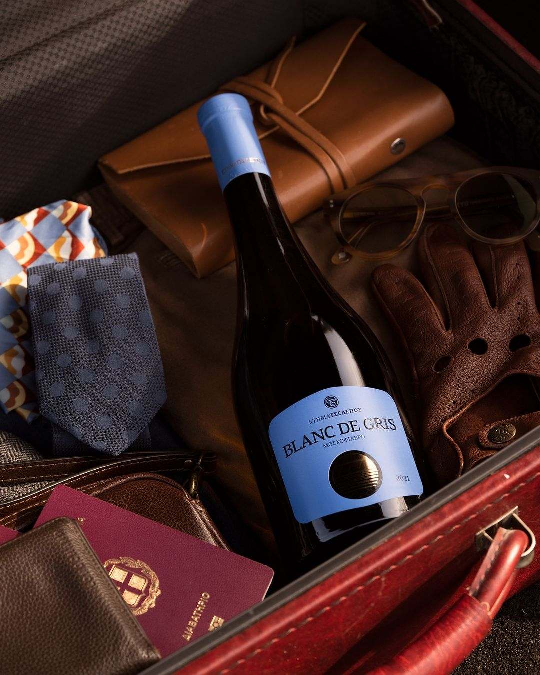 Flasche Blanc de Gris Wein 2023 mit blauer Etikettierung neben Accessoires in offenem Koffer