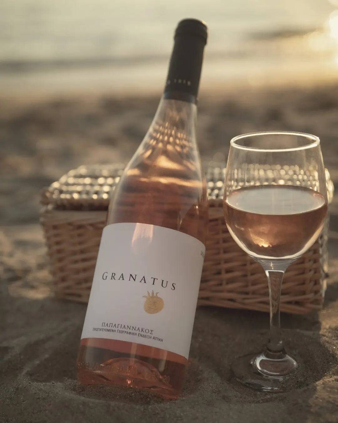 Papagiannakos Granatus Rosé Weinflasche und Glas in Lachsrosa am Strand mit Picknickkorb