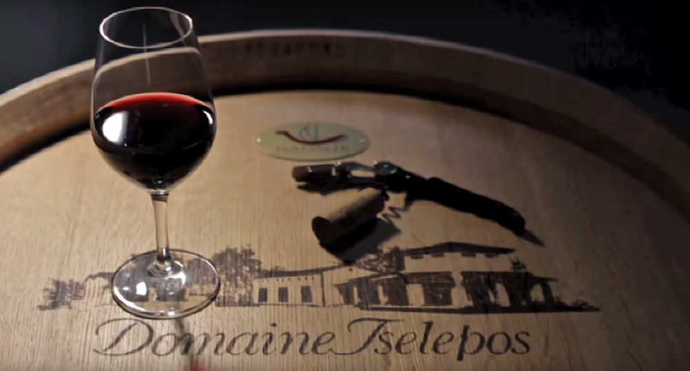 Rotwein in einem Weinglas auf einem Holzfass mit dem Logo von Domaine Iselepos
