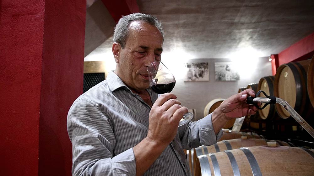 Mann mit Glas Rotwein in Weinkeller, umgeben von Holzfässern.