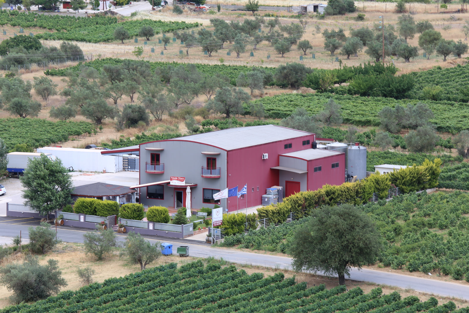 Weingut mit rotem Gebäude und grünen Weinreben im Vordergrund
