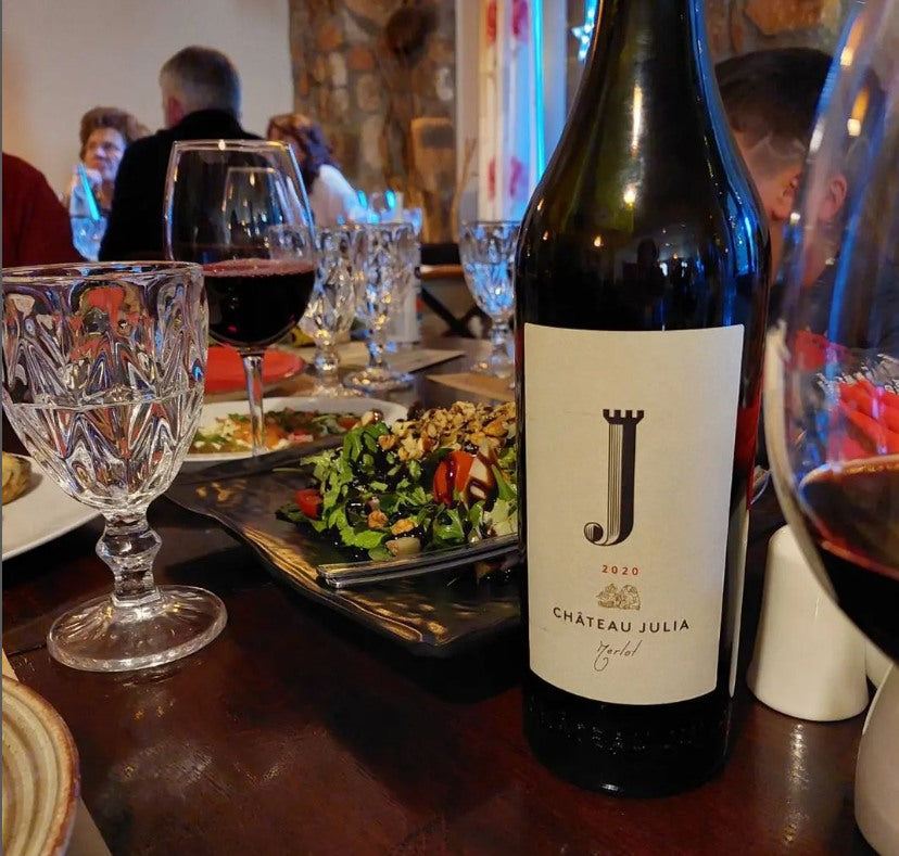 Chateau Julia Merlot 2020 Flasche neben Weinglas und Salat auf Restauranttisch