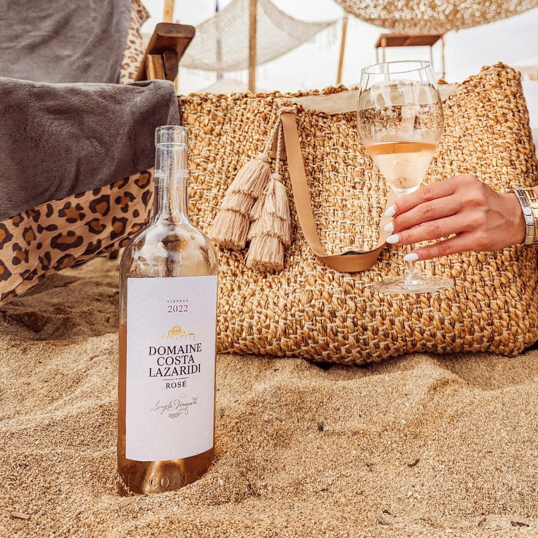 Domaine Costa Lazaridi Rosé Weinflasche und Glas mit hellem roséwein am Strand mit Strandtasche im Hintergrund