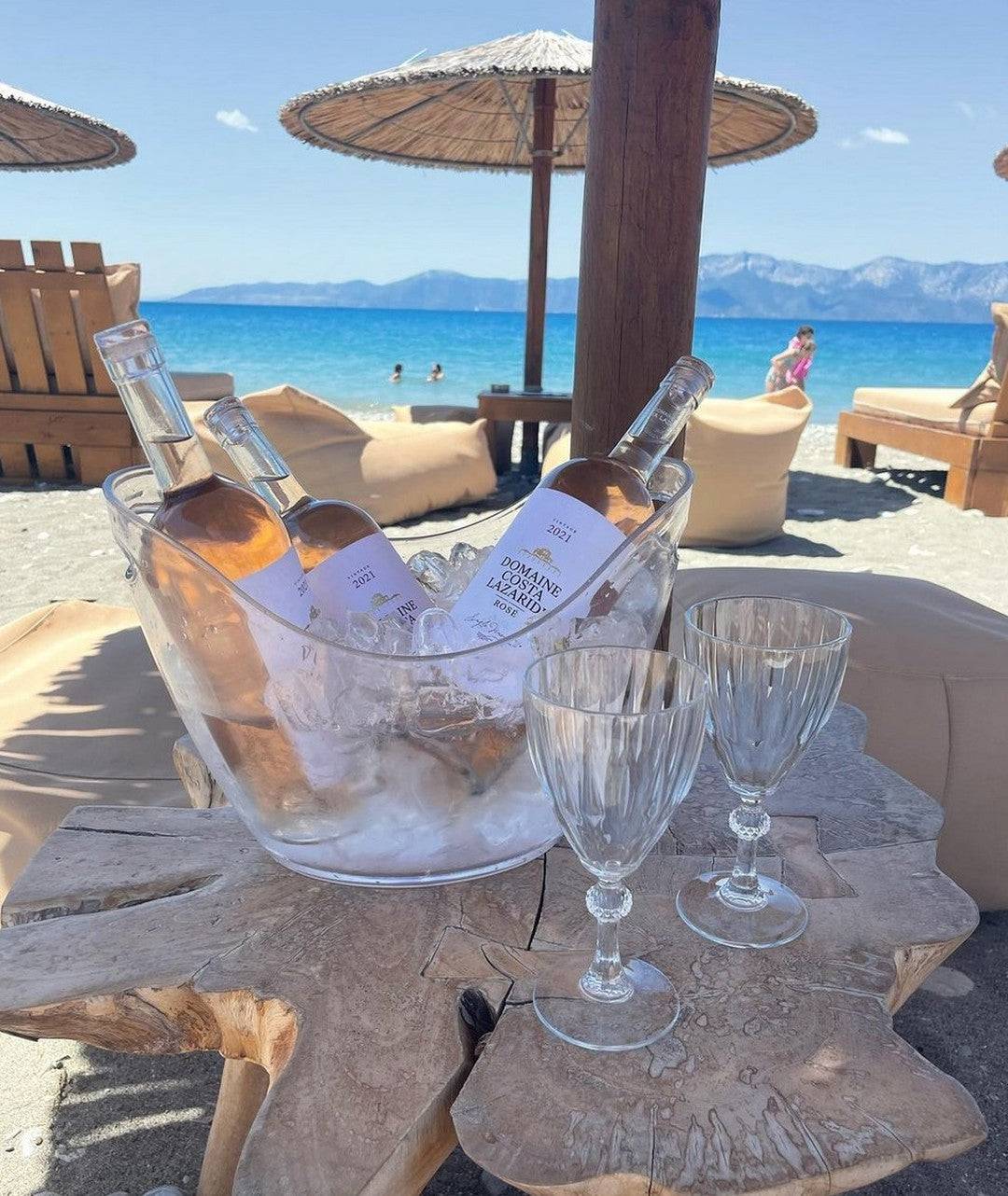 Flasche Malagousia Domaine Costa Lazaridi Weißwein 2024 im Eisbehälter am Strand mit Gläsern