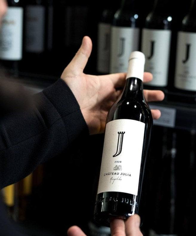 Flasche Chateau Julia Assyrtiko Weißwein 2022 mit elegantem Etikett in Hand vor Weinregal