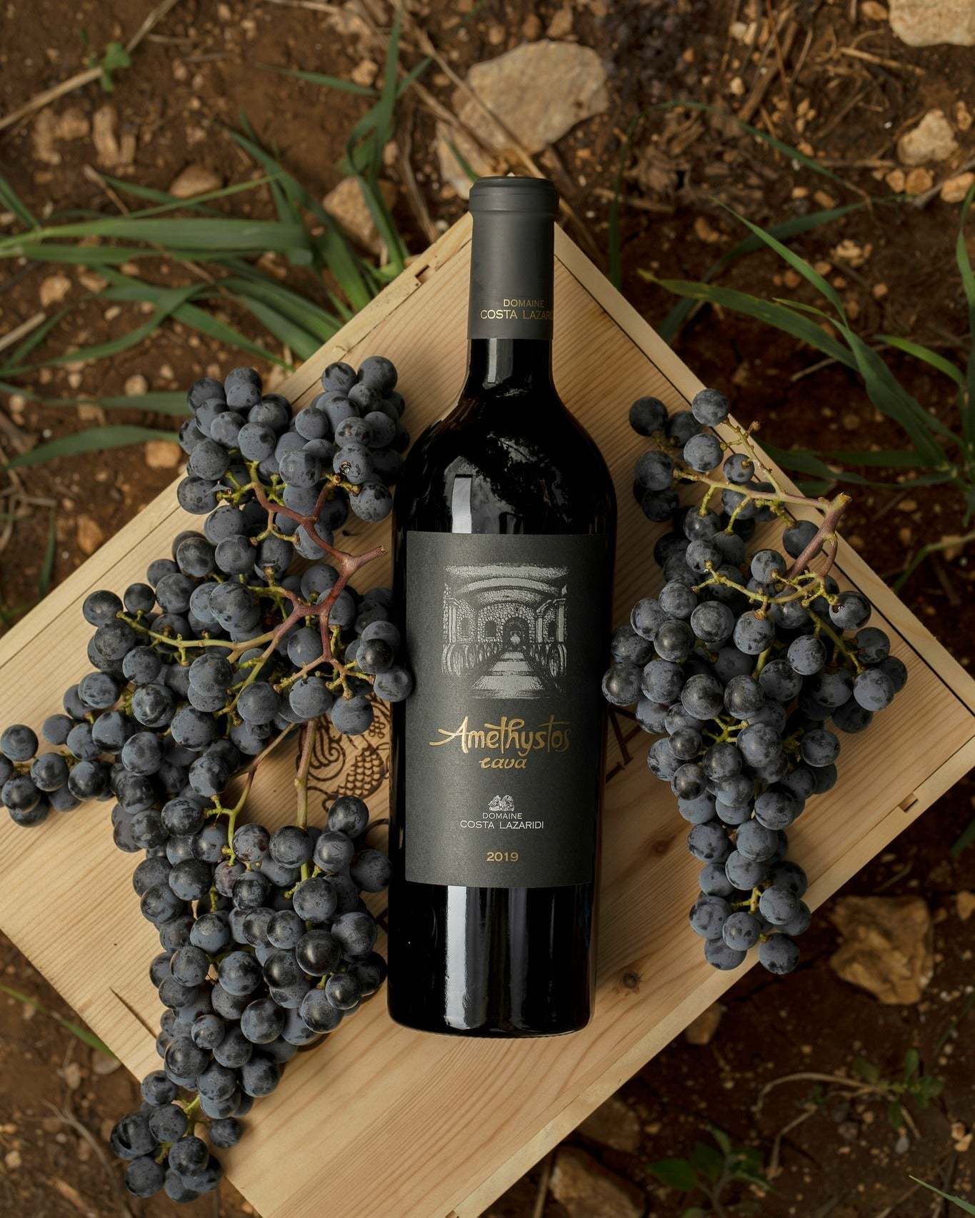 Flasche Amethystos Cava Rotwein 2019 umgeben von Trauben auf Holzkiste