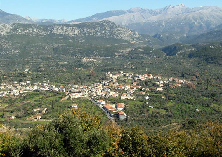 Landschaft mit einem kleinen Dorf umgeben von Bergen und Olivenhainen, blühende Natur und klare Sicht.