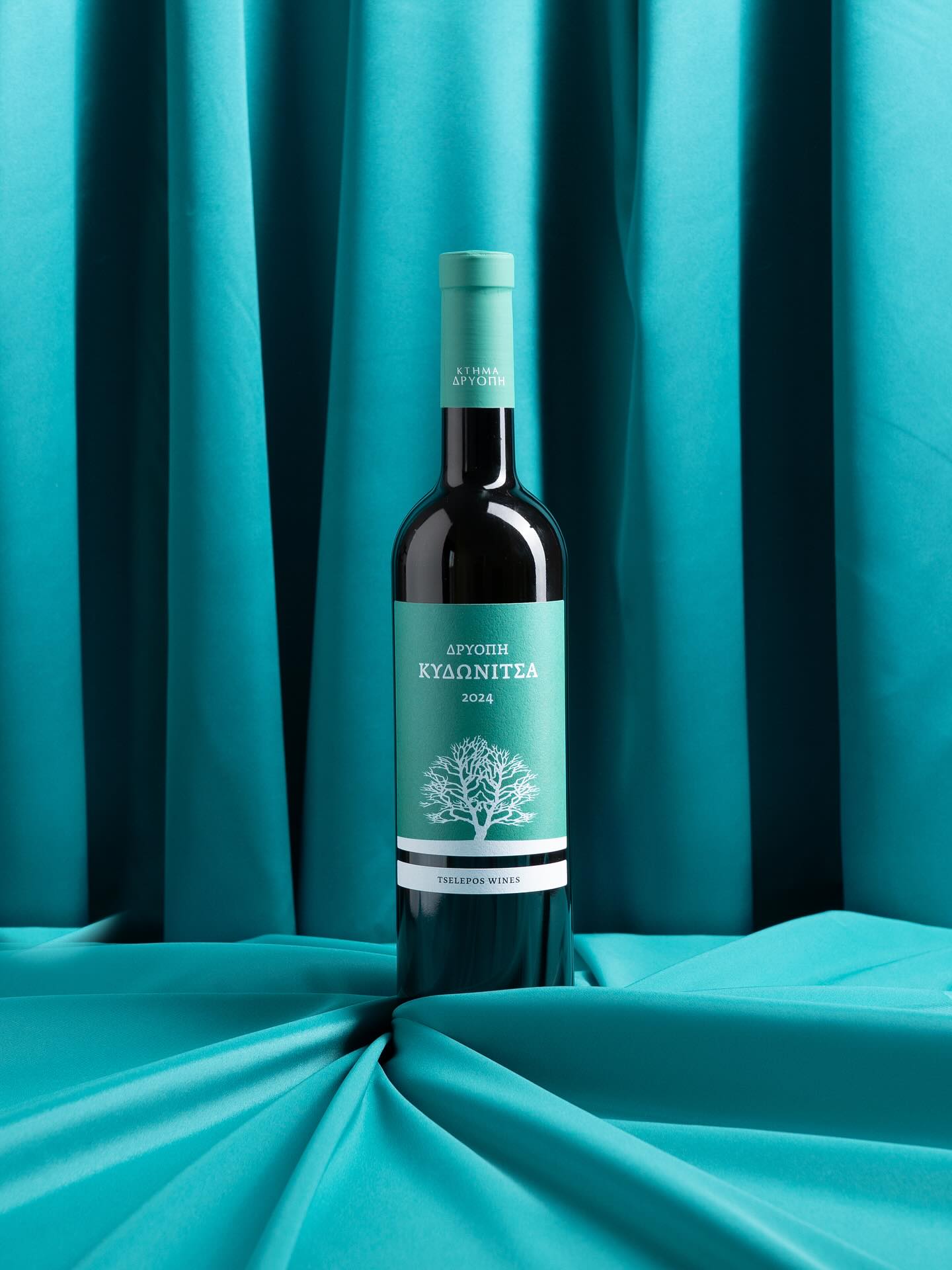 DRIOPI WINERY Kydonitsa Wein in einer eleganten Flasche, sortenrein und trocken, vor türkisfarbenem Hintergrund.