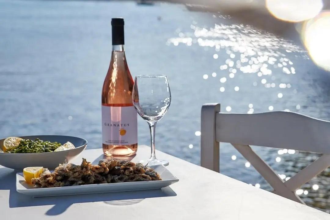 Papagiannakos Granatus Rosé Weinflasche mit Glas am Meeresspiegel auf weißem Tisch mit Meeresfrüchten und Salat