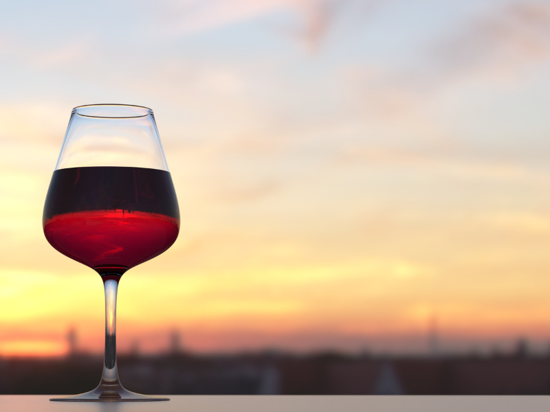 Rotweinglas mit rotem Wein vor einem Sonnenuntergang