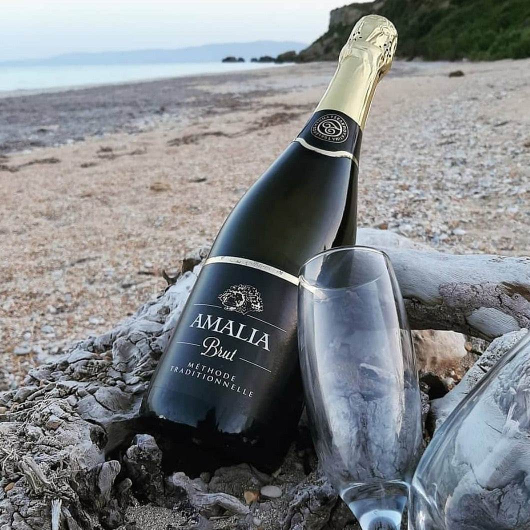 Flasche Amalia Brut Moscofilero Sekt mit zwei Gläsern am Strand liegend