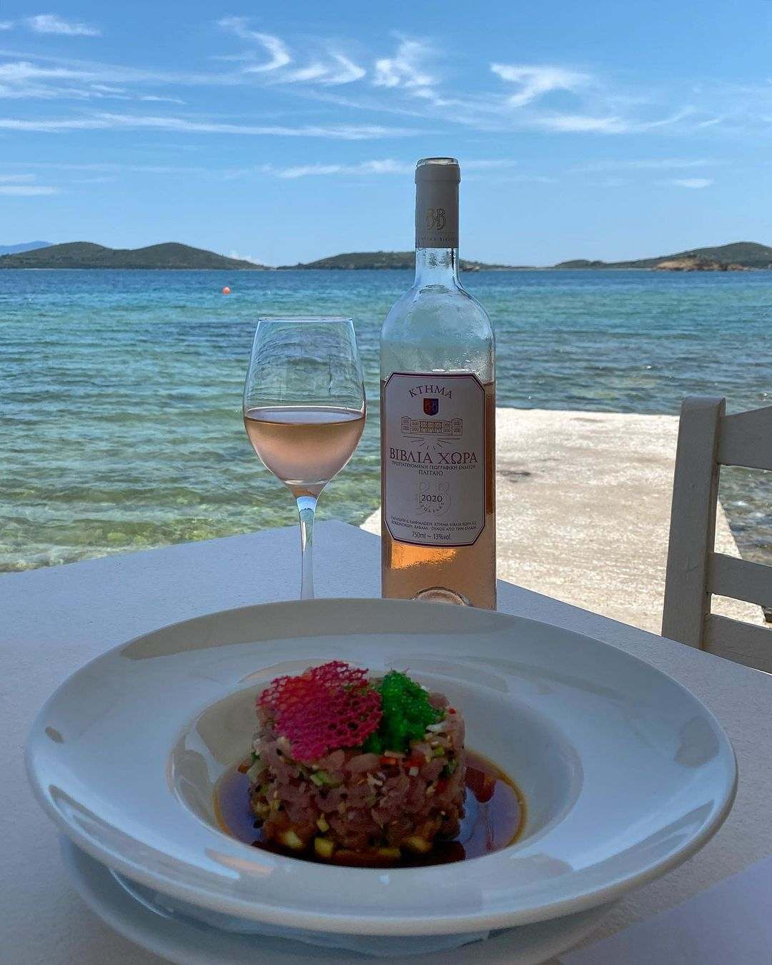 Biblia Chora Rosé Weinflasche und Glas am Meer mit exotischem Gericht auf weißem Teller