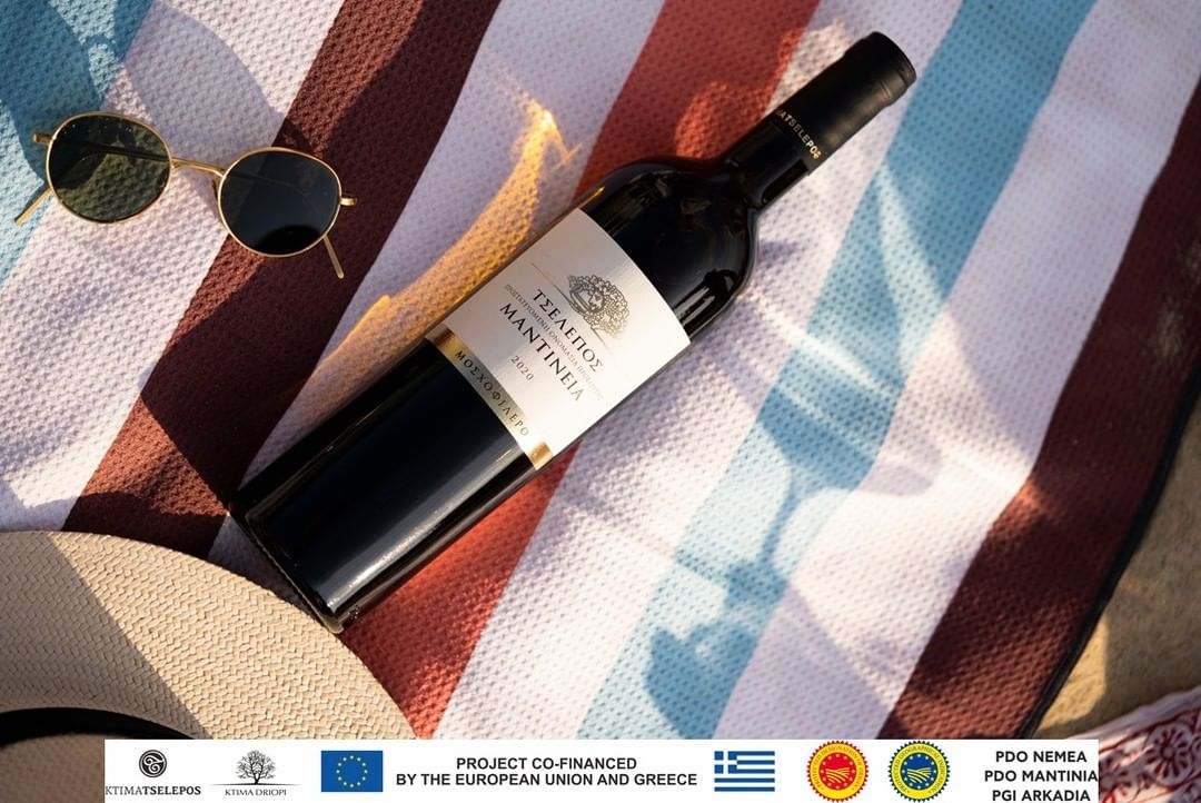 Flasche Tselepos Mantinia PDO Wein aus Moscofilero Trauben 2023 mit Sonnenbrille und Hut auf buntem Strandtuch