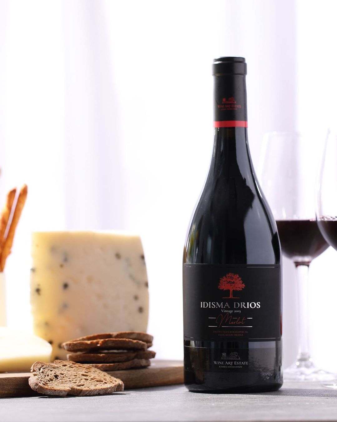 Idisma Drios Merlot 2021 Rotwein Flasche mit Käse, Brot und Rotweingläsern