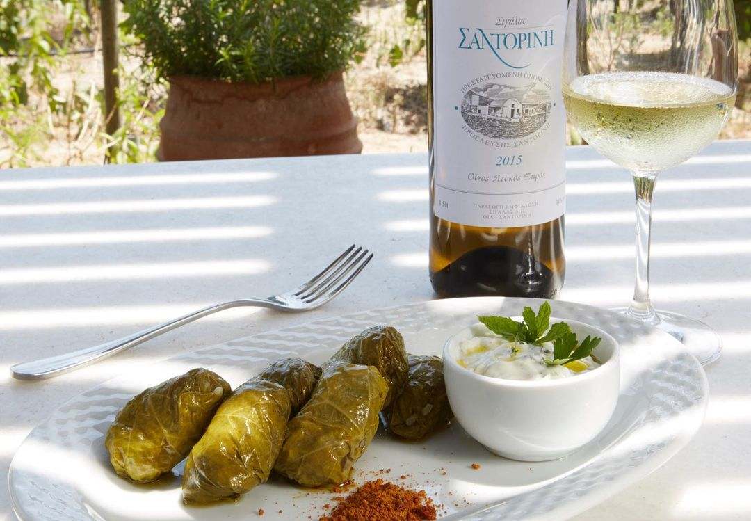 Flasche Sigalas Santorini Weißwein mit Glas und gefüllten Weinblättern auf Teller mit Dip