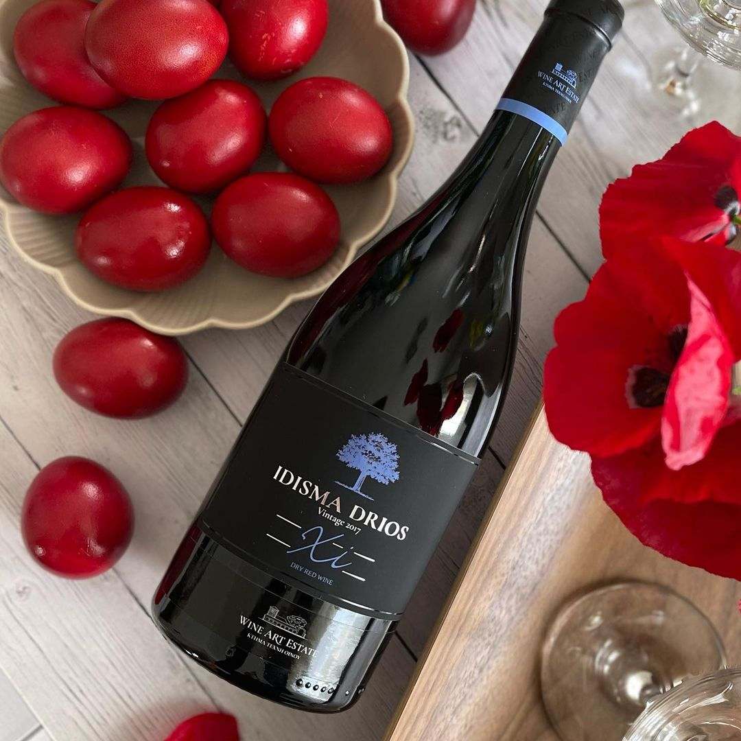 Flasche Idisma Drios Xinomavro Rotwein aus Drama PGI mit roten Eiern und Mohnblume auf Holztisch