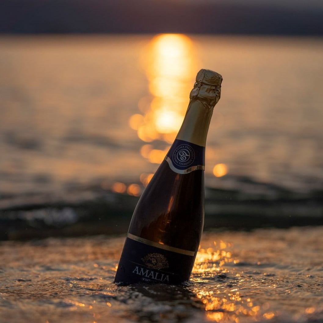 Amalia Brut Schaumweinflasche mit goldgelbem Schimmer im Wasser bei Sonnenuntergang