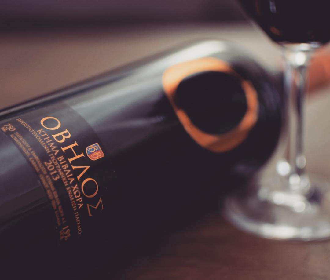Ovilos Red Cabernet Sauvignon 2020 Weinflasche neben Weinglas mit tiefrotem Wein auf Holztisch