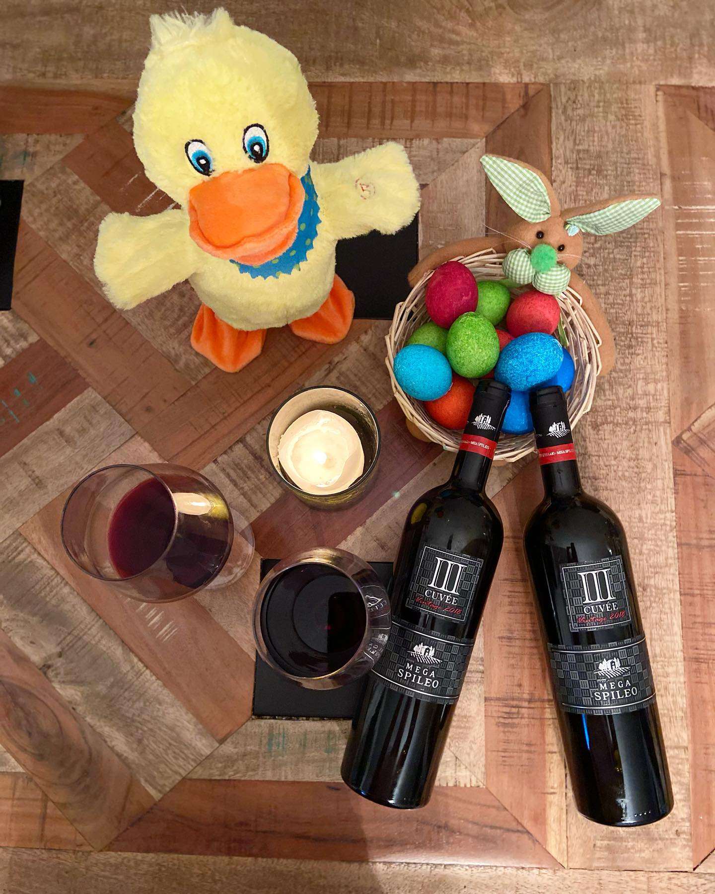 Mega Spileo Cuvee III Rot Weinflaschen mit zwei gefüllten Weingläsern und Osterdekoration auf Holztisch
