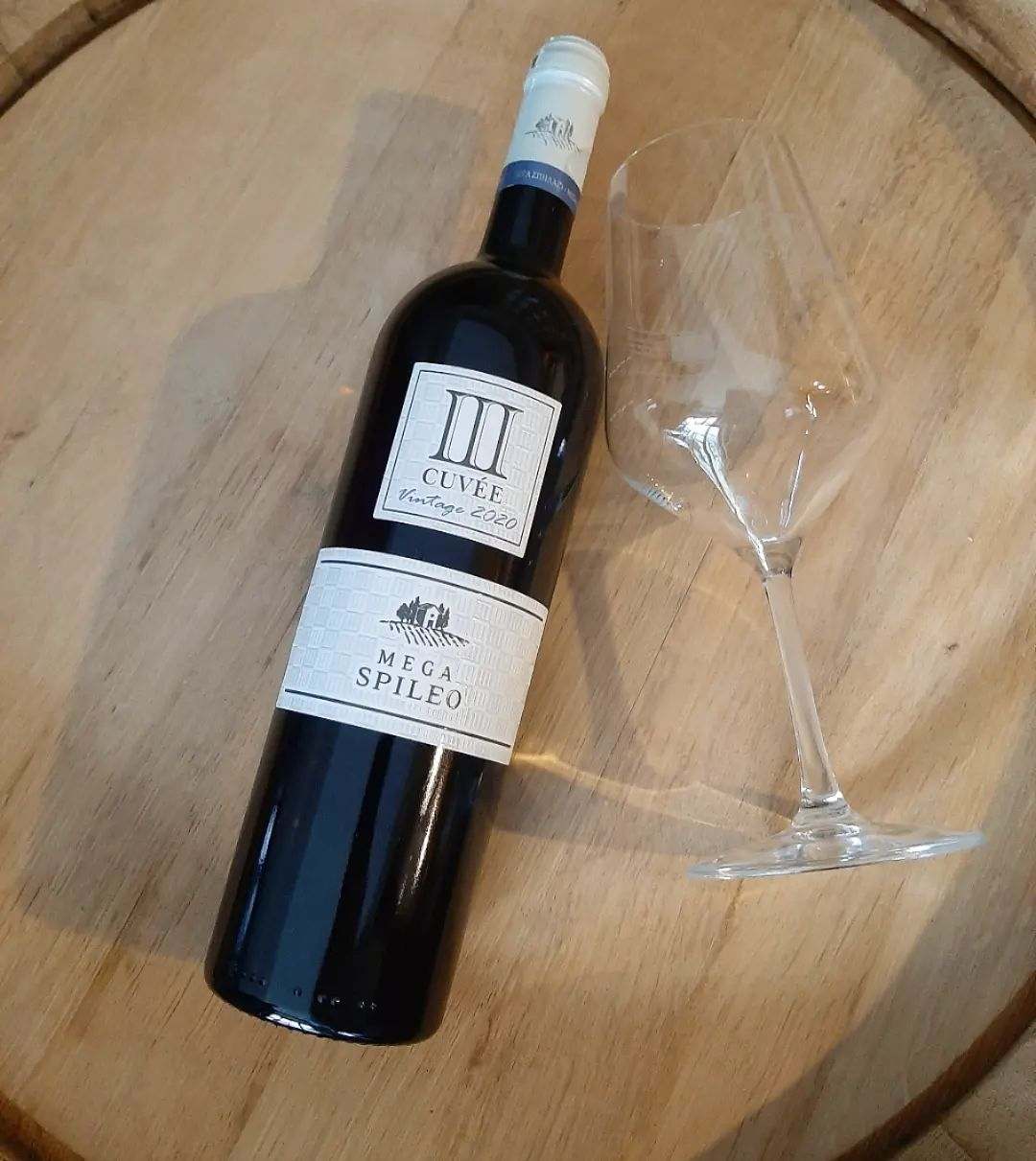 Mega Spileo Cuvee III Weißweinflasche mit Weinglas auf Holztisch