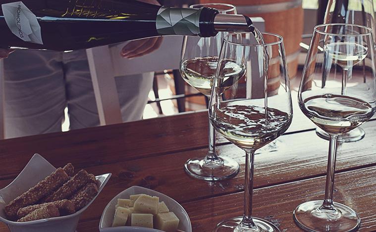Weißwein in einer Flasche wird in Gläser gegossen, auf einem Holztisch mit Snacks.