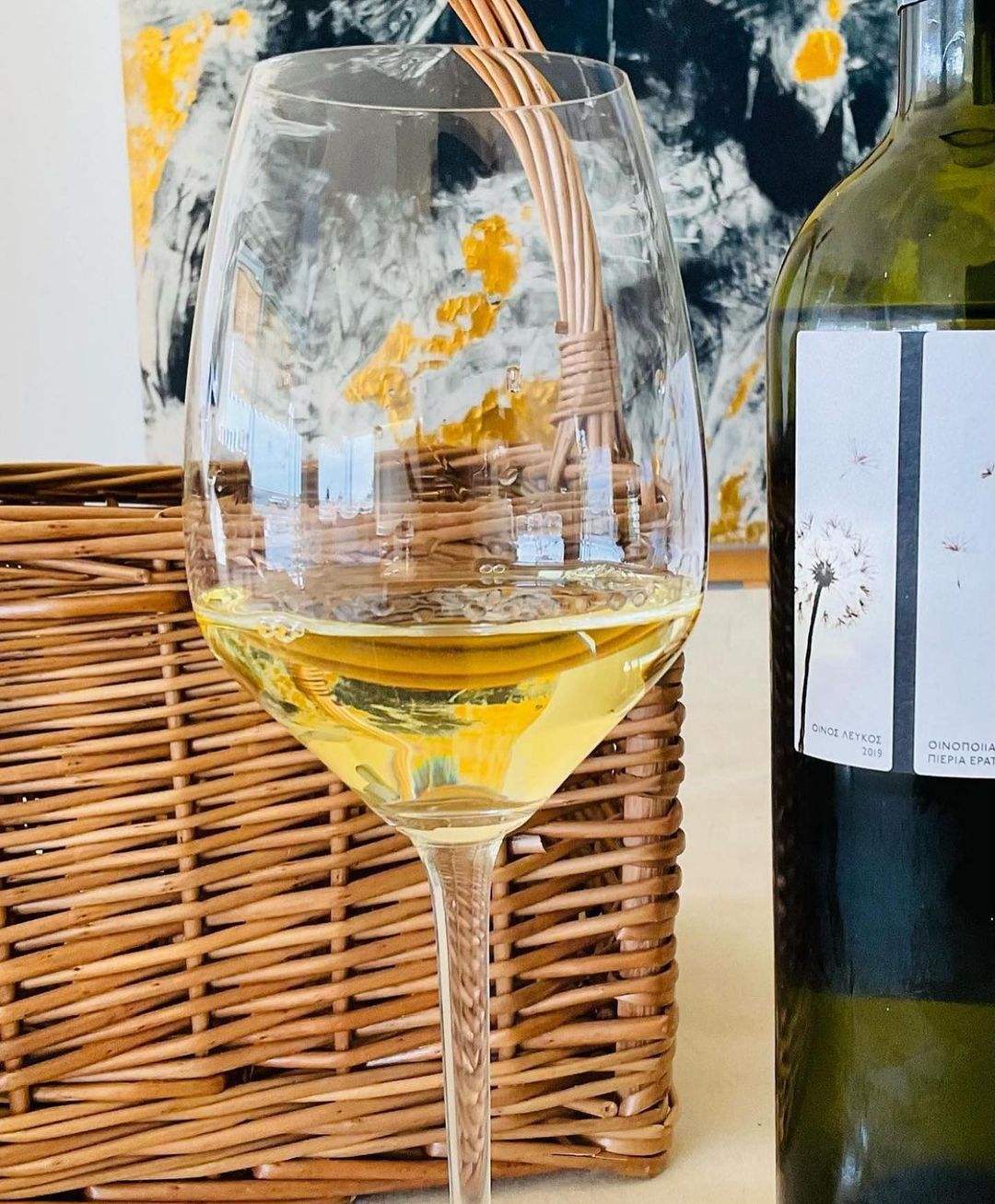 Weißwein Evches White von PIERIA ERATINI in einem Glaskelch mit goldenen Reflexen und einem Weidenkorb im Hintergrund