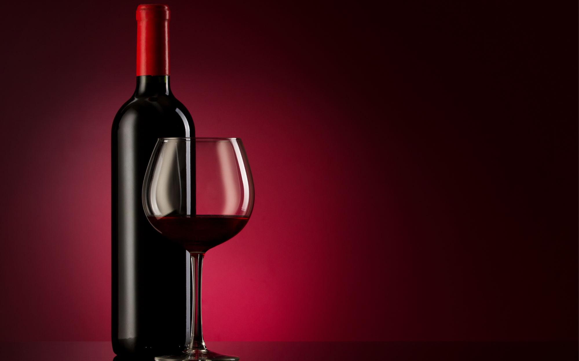 Rotweinflasche mit rotem Korken und Weinglas mit Rotwein auf rotem Hintergrund