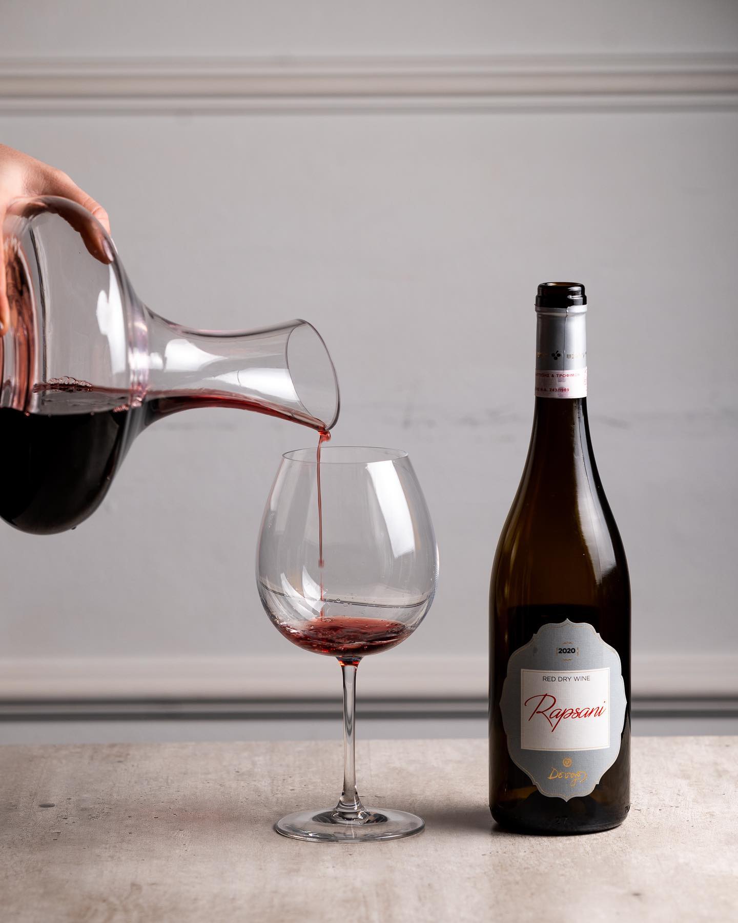 Rotwein aus einer Glaskaraffe in ein großes Weinglas mit Etikett von Reggiani 2020.