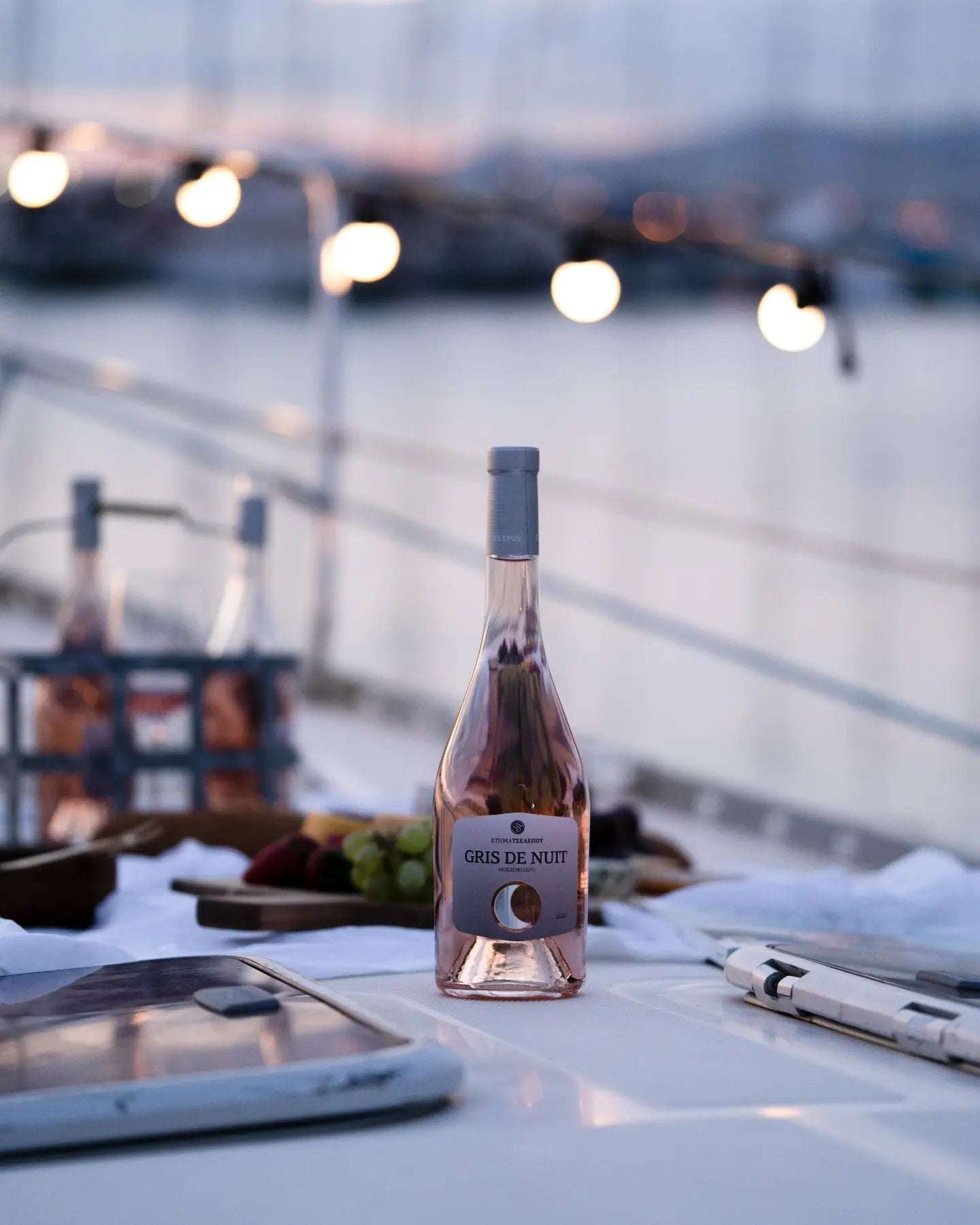 Roséwein Domaine Tselepos Gris de Nuit in einer eleganten Flasche auf einem Tisch mit Früchten und maritimem Hintergrund