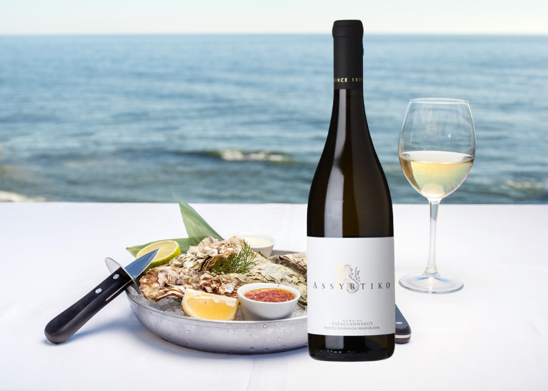 Weißwein Assyrtiko in Flasche mit Glas, serviert mit Austern und Zitronen auf einem Tisch am Meer.