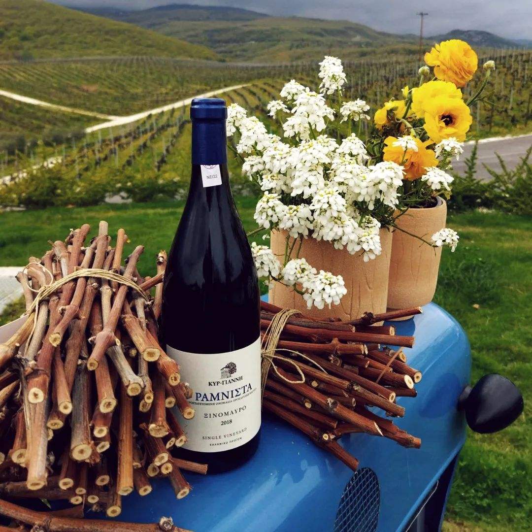Rotwein Kir Yianni Ramnista Jahrgang 2019 aus Xinomavro auf einer rustikalen Unterlage mit Blumenarrangement