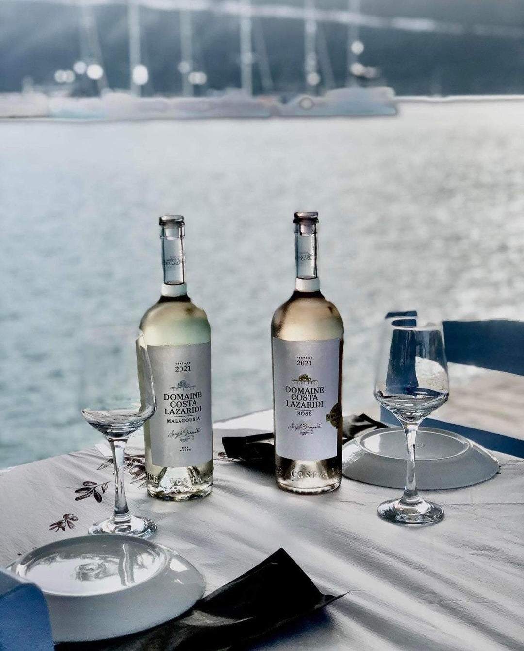 Domaine Costa Lazaridi Rosé Weinflaschen mit Gläsern am Tisch vor Meerblick