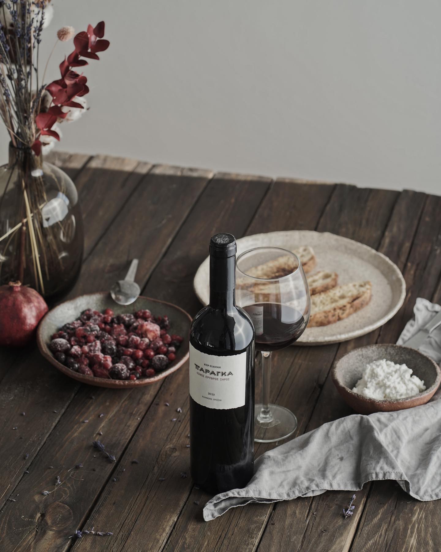 Rotwein in einer Glasflasche mit Etikett, serviert mit Obst und Gebäck auf einem Holztisch.