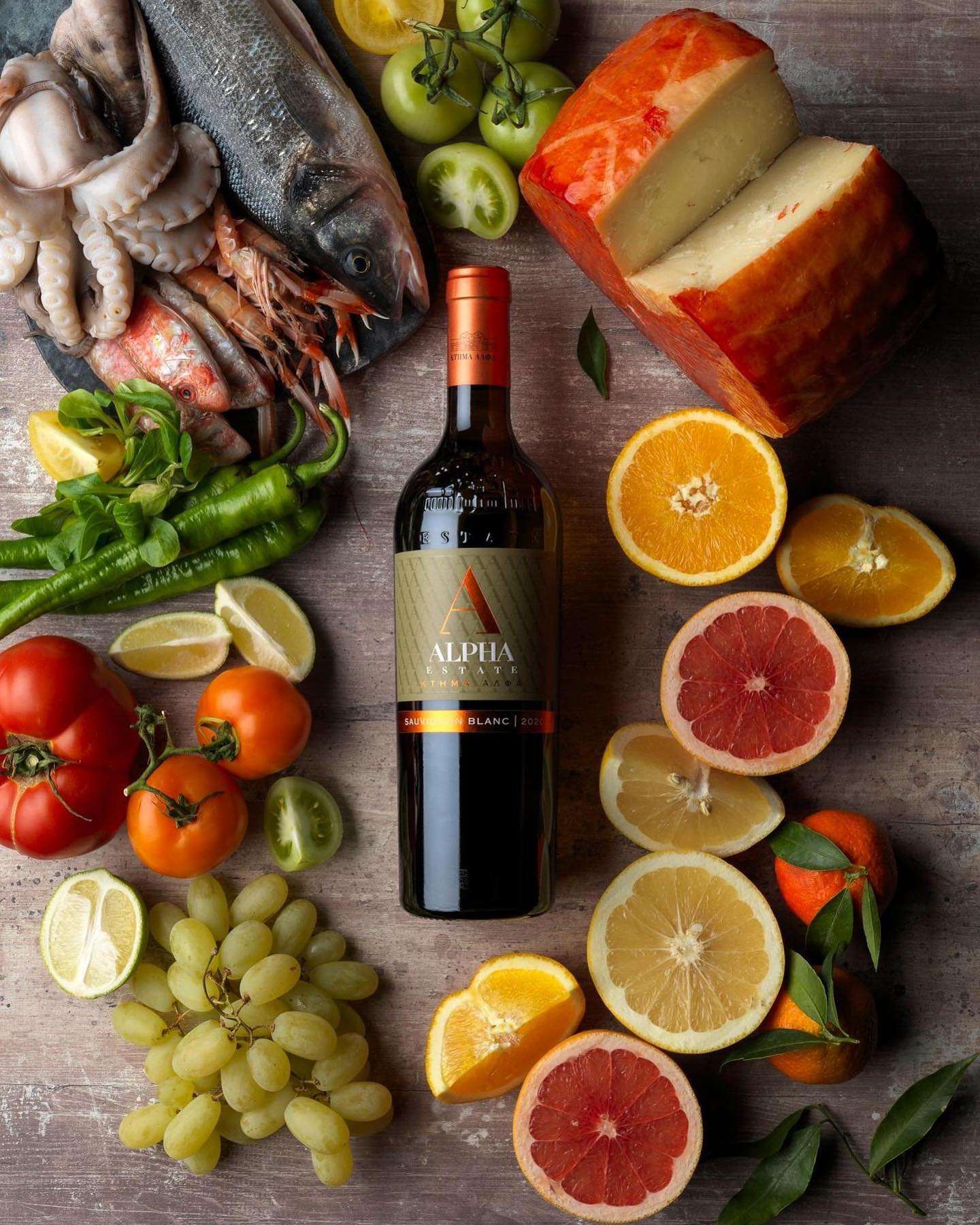 Flasche Alpha Estate Sauvignon Blanc mit frischen Früchten, Käse und Meeresfrüchten auf Holzoberfläche
