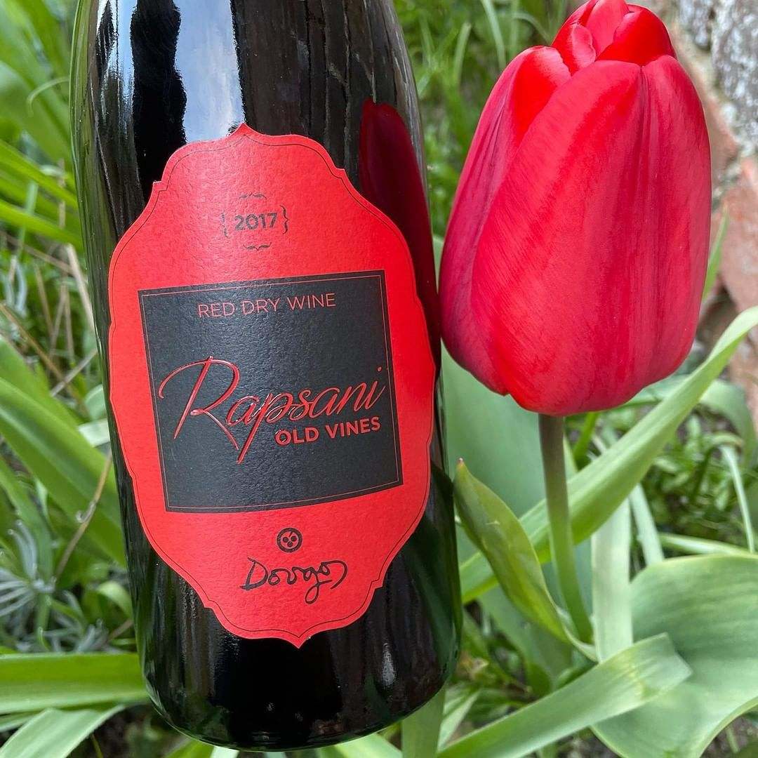 Dougos Rapsani Old Vines Rotwein Flasche mit rotem Etikett und roter Tulpe im Garten