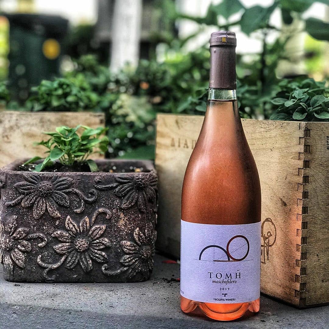 Rosé-Flasche mit dem Etikett &quot;Troupis Winery Tomi Rosé&quot; vor einem Blumentopf und anderen Dekorationselementen